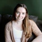 Abigael Davis, LCSW, Trauma Therapist with light brown hair, smiling sitting on a gray couch wearing a white shirt and cream cardigan.