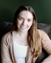Abigael Davis, LCSW, Trauma Therapist with light brown hair, smiling sitting on a gray couch wearing a white shirt and cream cardigan.