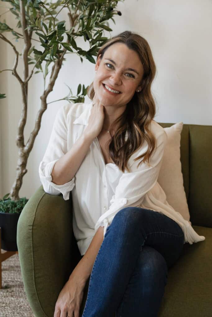 Woman therapist in a white shirt sitting on a couch smiling warmly.