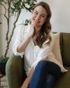 Woman therapist in a white shirt sitting on a couch smiling warmly.